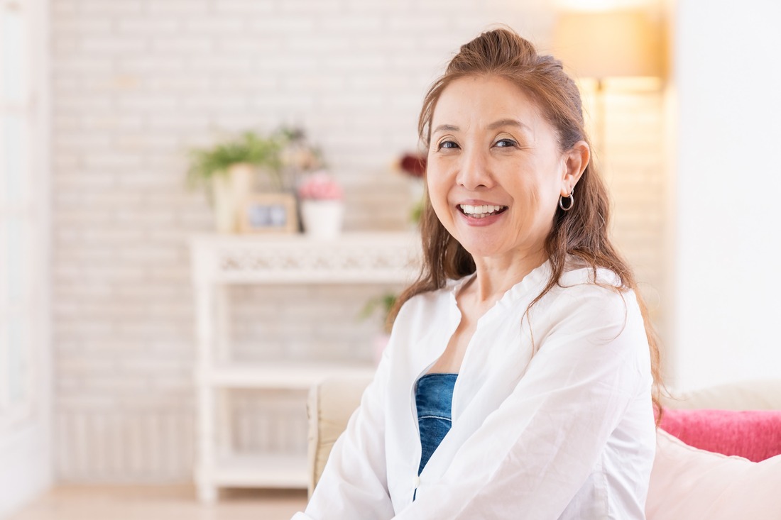 An older Asian woman with a warm smile sits comfortably indoors.