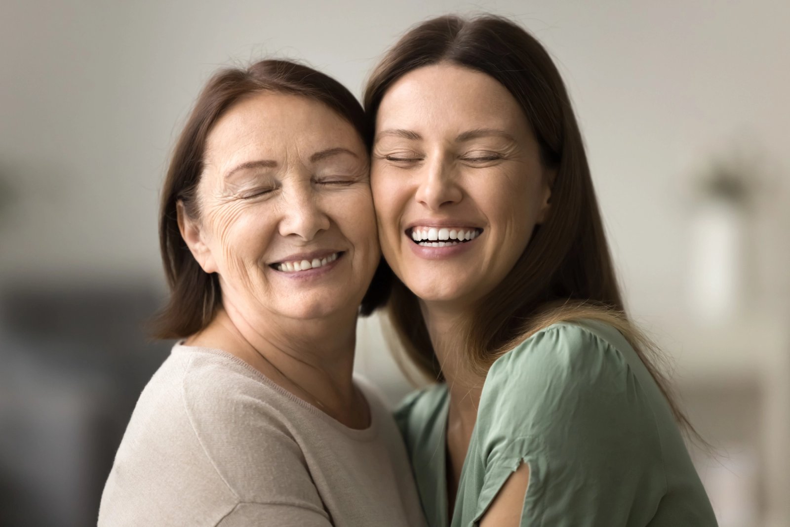Smiling mother and daughter with closed eyes and heads touching.