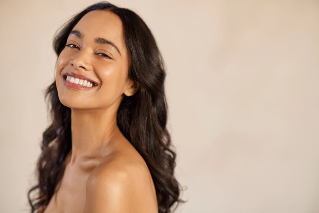 A smiling woman with dark, wavy hair and bare shoulders looks at the camera.