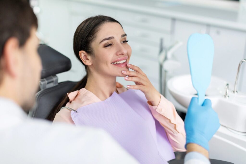 Woman in dentist's chair smiling happily at her reflection in a mirror.