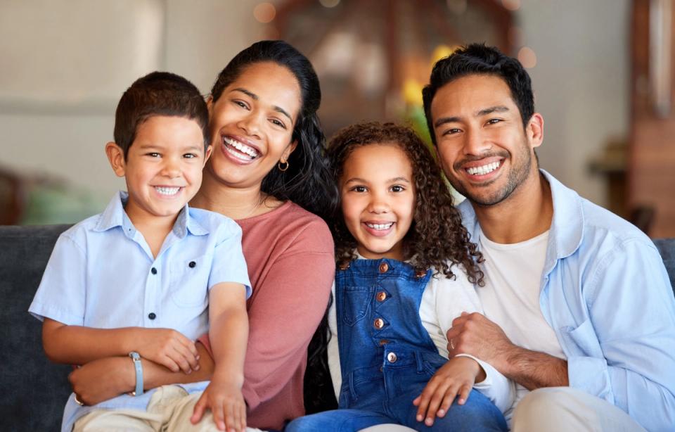 A smiling family of four, including two parents and two children, sitting together.