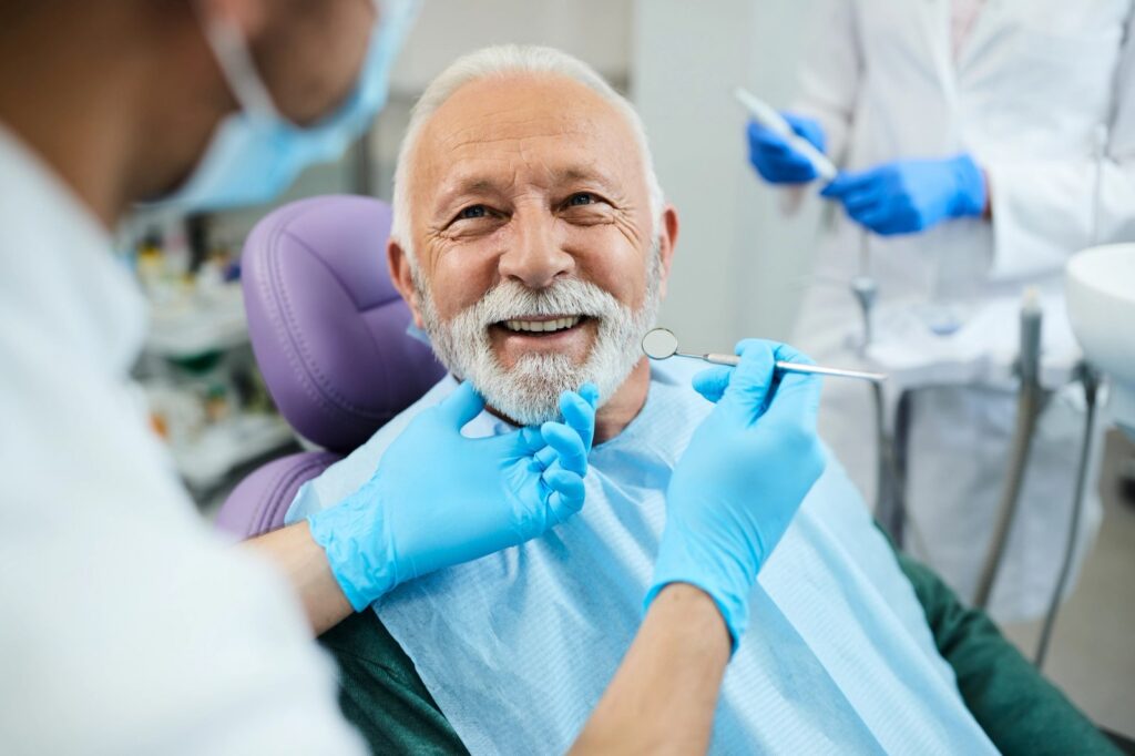 Dental Crowns and Bridges: What’s the Real Difference? an elderly man is sitting in a dental chair while a dentist examines his teeth .