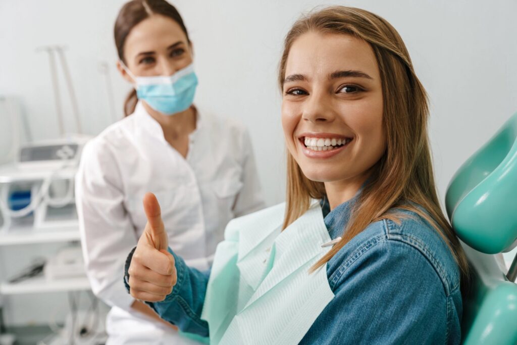 Solving Problems with Dental Veneers Easily a woman is sitting in a dental chair and giving a thumbs up.