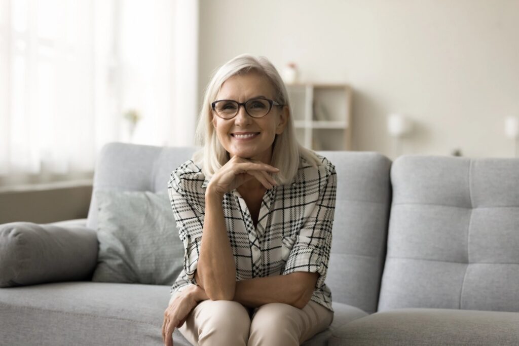 All-on-5 Implants: Five Implants, One Secure Full-Arch Smile an elderly woman is sitting on a couch wearing glasses and smiling .