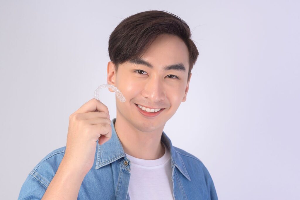 Transform Your Smile Discreetly: The Remarkable Benefits of Invisalign Clear Aligners a young man is holding a clear brace on his teeth .
