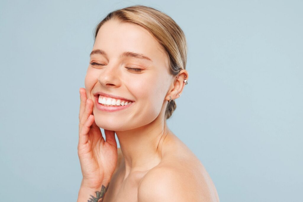 Implant Bridges In Trinity: Reliable Tooth Replacement Without Wearing A Removable Partial A smiling woman with closed eyes touches her cheek.