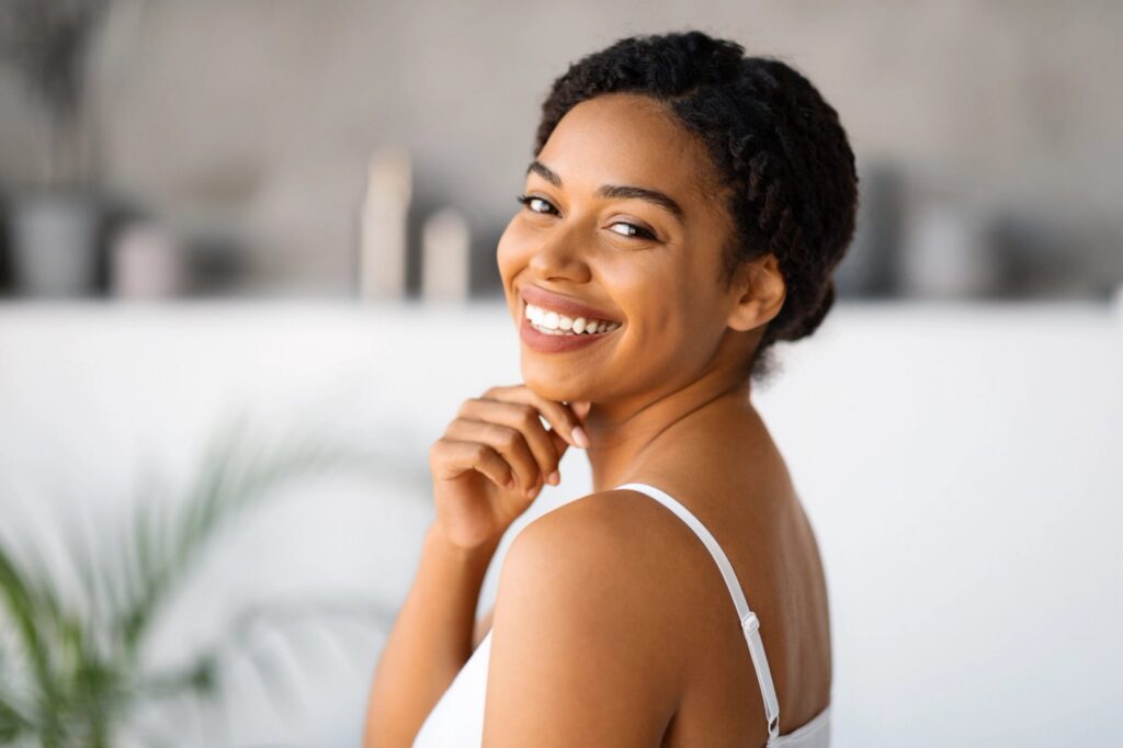 Dental Implants In Trinity: A Natural-Feeling Way To Replace Missing Teeth A smiling Black woman in a white camisole looks over her shoulder.