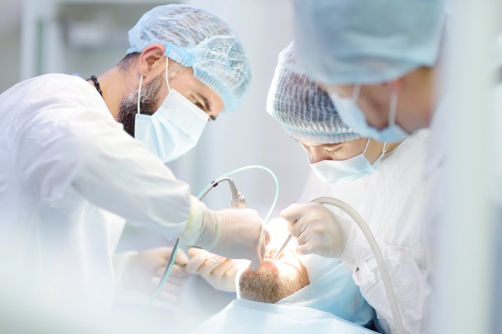 Two medical professionals in scrubs operating on a patient's mouth.