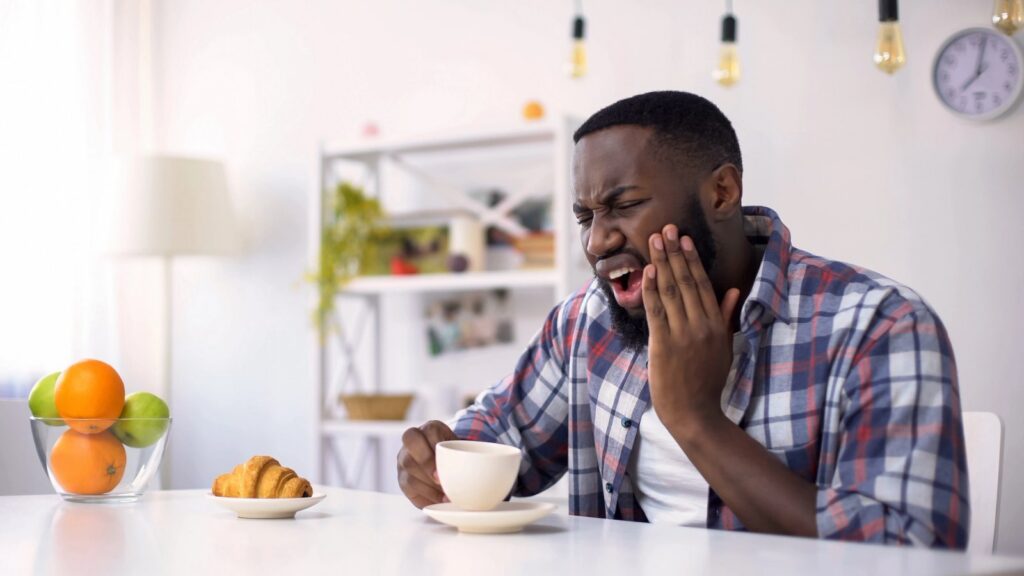 Emergency Dentistry: Same-Day Care and Smart Ways to Avoid Tooth Injuries a man is sitting at a table with a cup of coffee and a croissant .