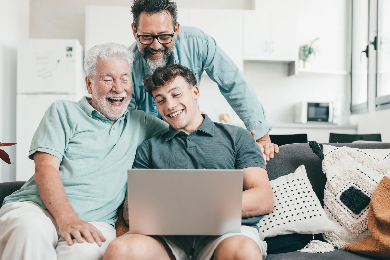 Three men of different generations laugh together while looking at a laptop.
