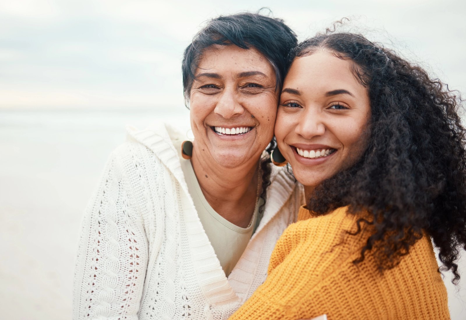 Two smiling women, an older and a younger, embracing on a beach.
