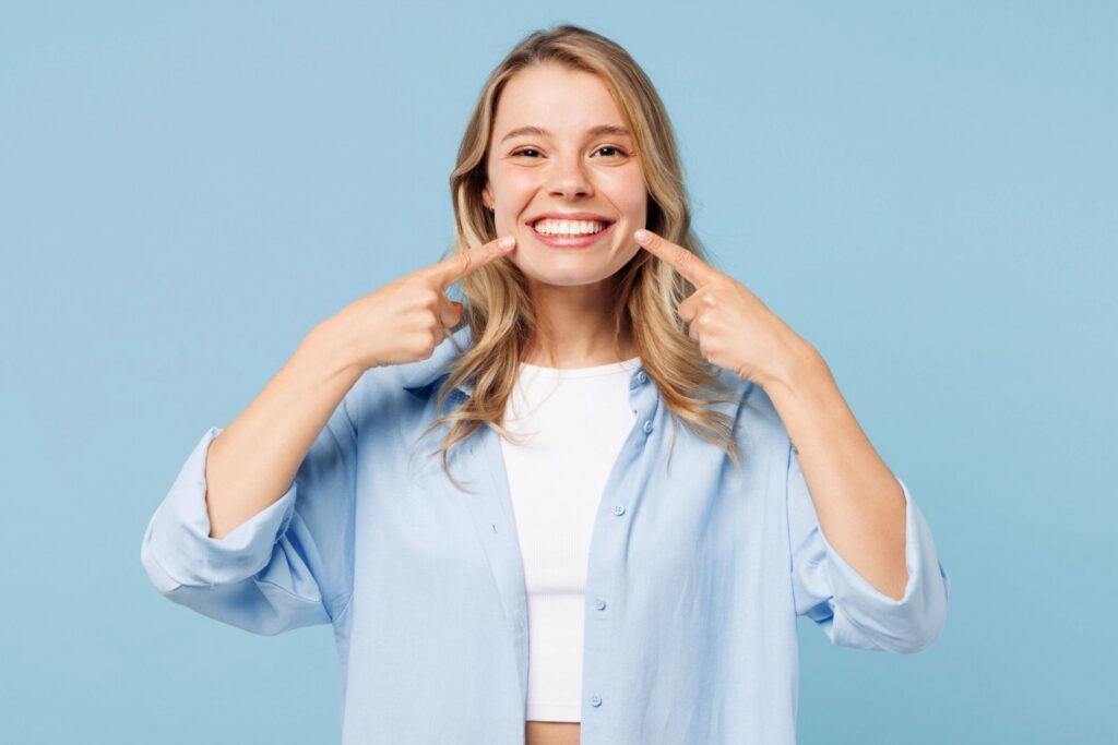 a woman is pointing at her teeth and smiling .