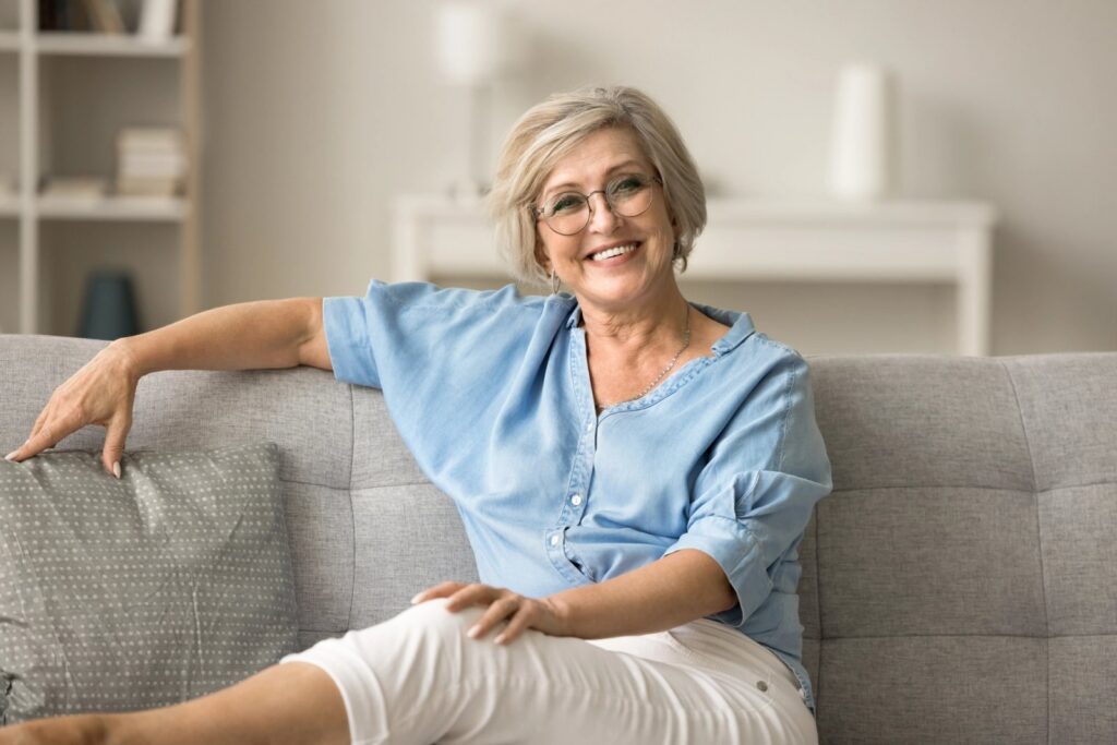 Implant Bridges: A Strong, Natural-Looking Way to Replace Multiple Missing Teeth an older woman is sitting on a couch with her legs crossed and smiling .