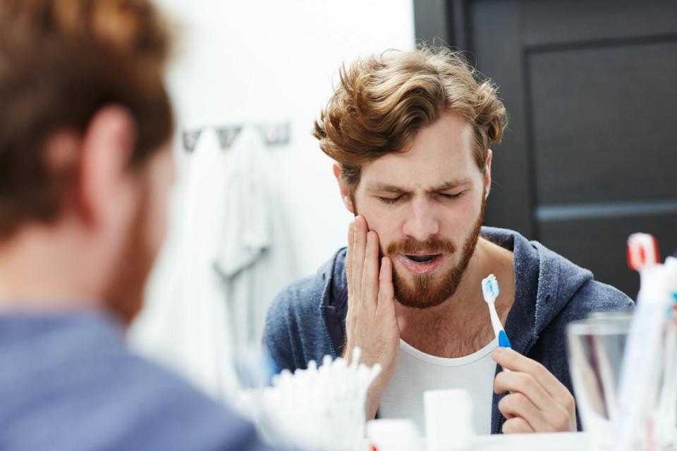 a man is brushing his teeth in front of a mirror and has a toothache.